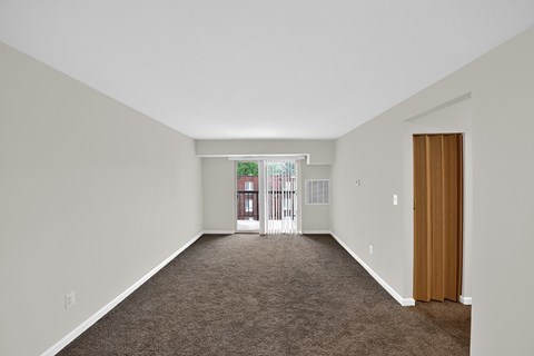 a spacious living room with carpet and a door to a balcony